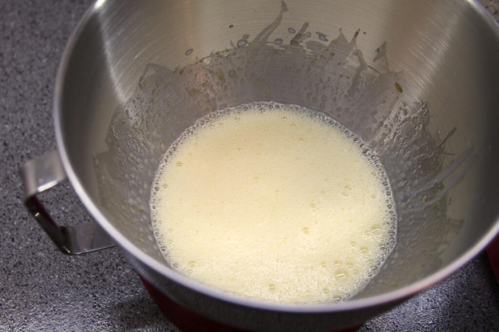 A mixture of egg, sugar, and milk in the bowl of a stand mixer.