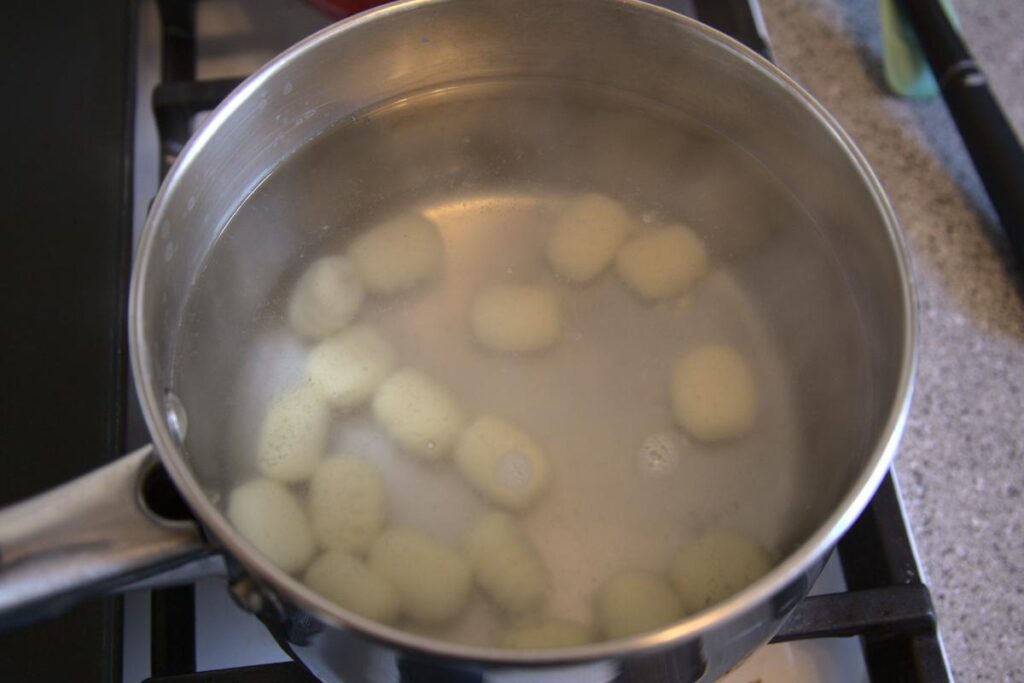 Gnocchi cooking in a pot of water on the stove, the gnocchi are at the bottom of the pot