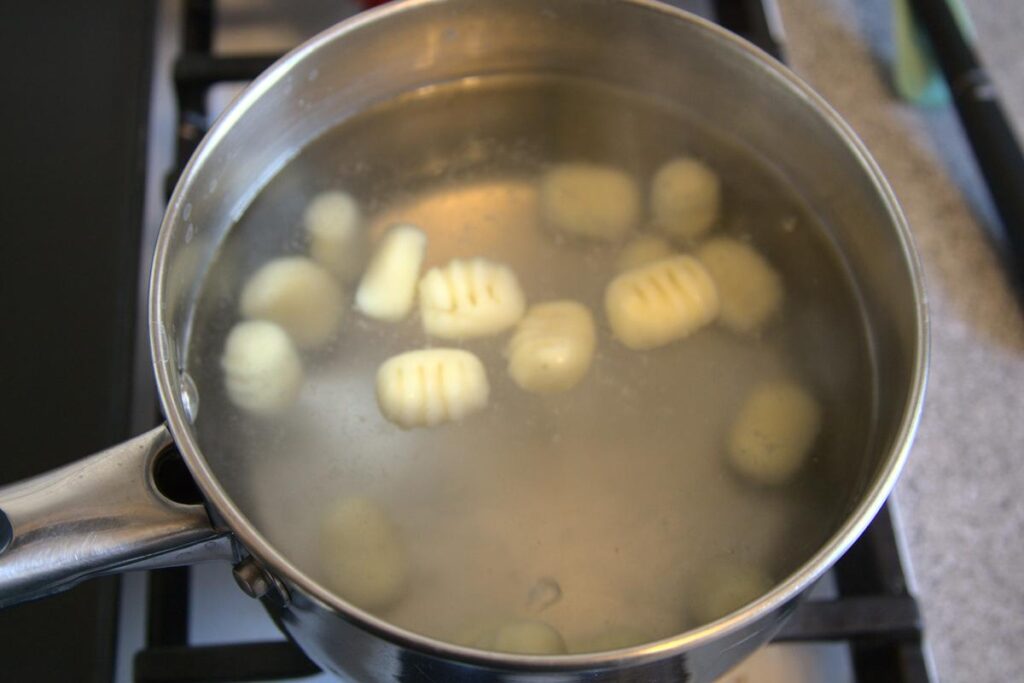 Gnocchi cooking in a pot of water on the stove, the gnocchi are just starting to float