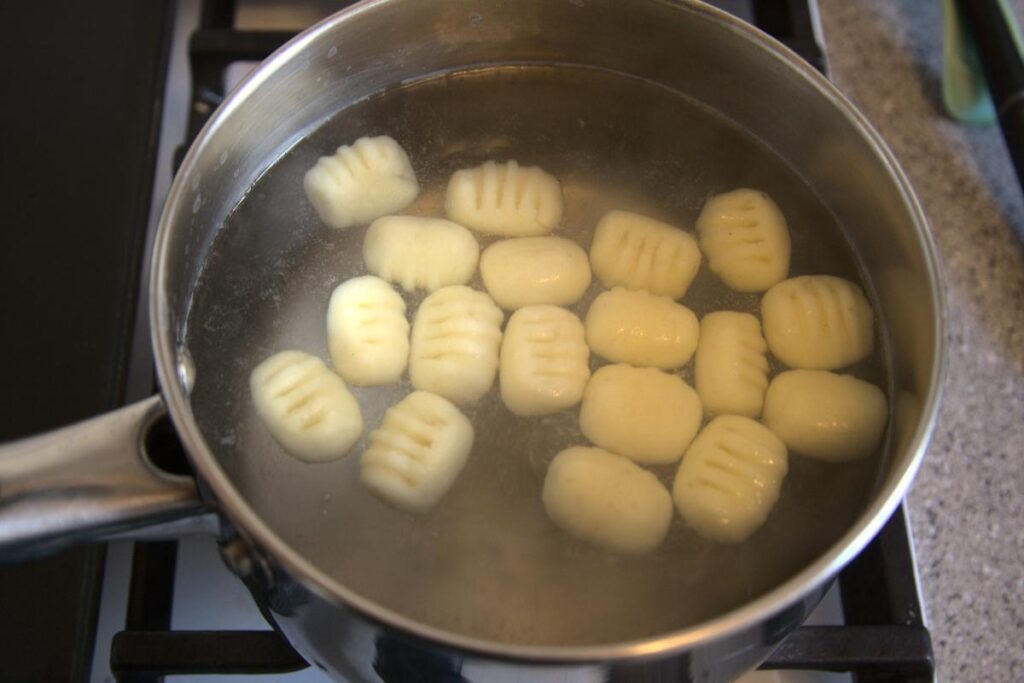 Gnocchi cooking in a pot of water on the stove, the gnocchi are all floating at the top showing they are cooked