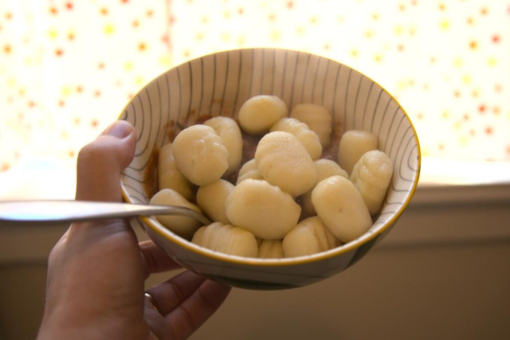 A hand holds a small bowl of cooked gnocchi.