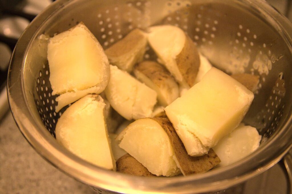 Cooked potato chunks in a colander, the potato skins are loose.