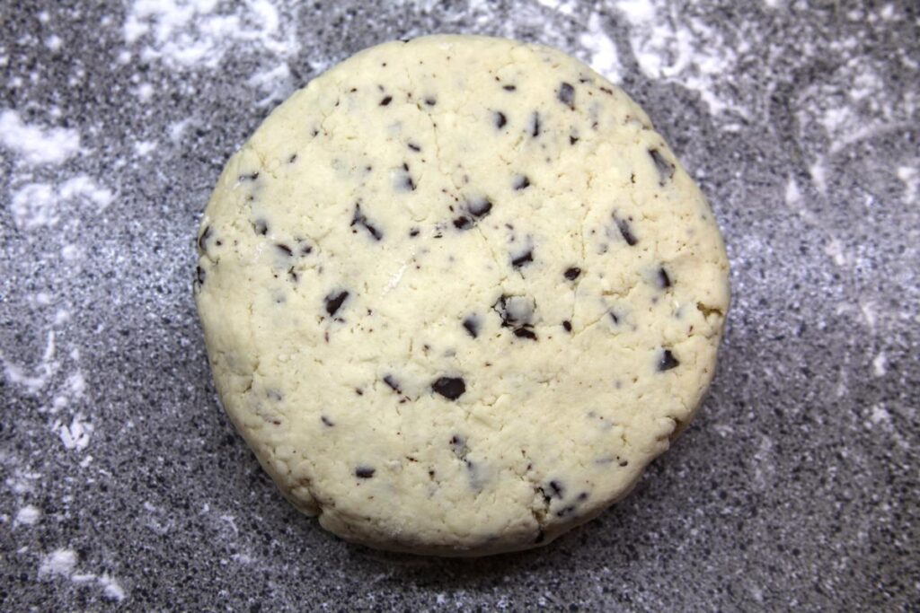Chocolate chunk scone dough is sitting on a floured countertop and has been shaped into a flat disk 6 inches in diameter.