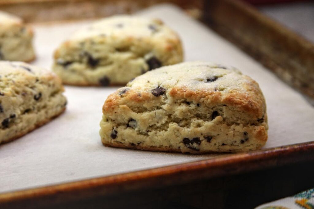 A close-up of baked scones on a parchment lined baking sheet. The edges of the scone are lightly browned.