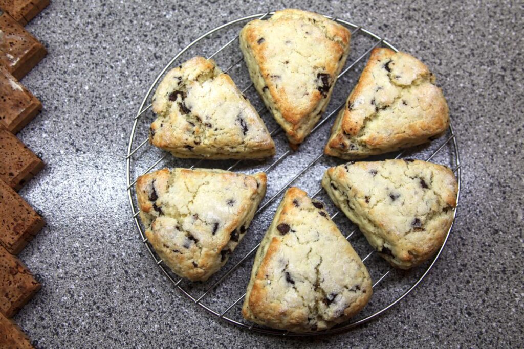 Six chocolate chunk scones in a circle cooling on a rack on a grey countertop.