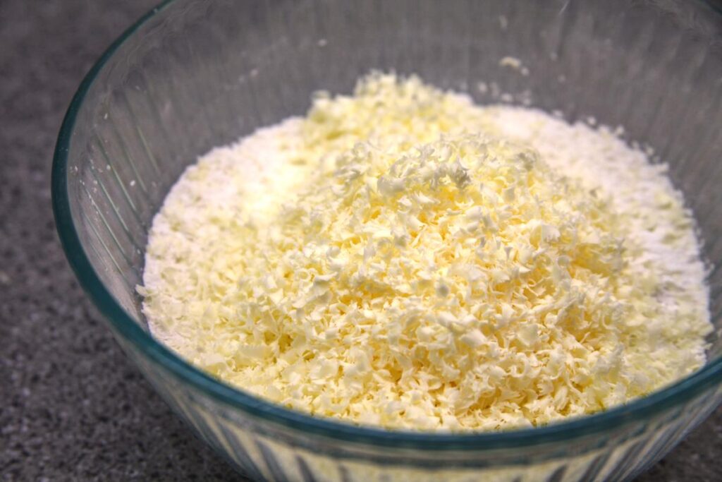 A close-up shot of a bowl of flour with grated butter on top of it.