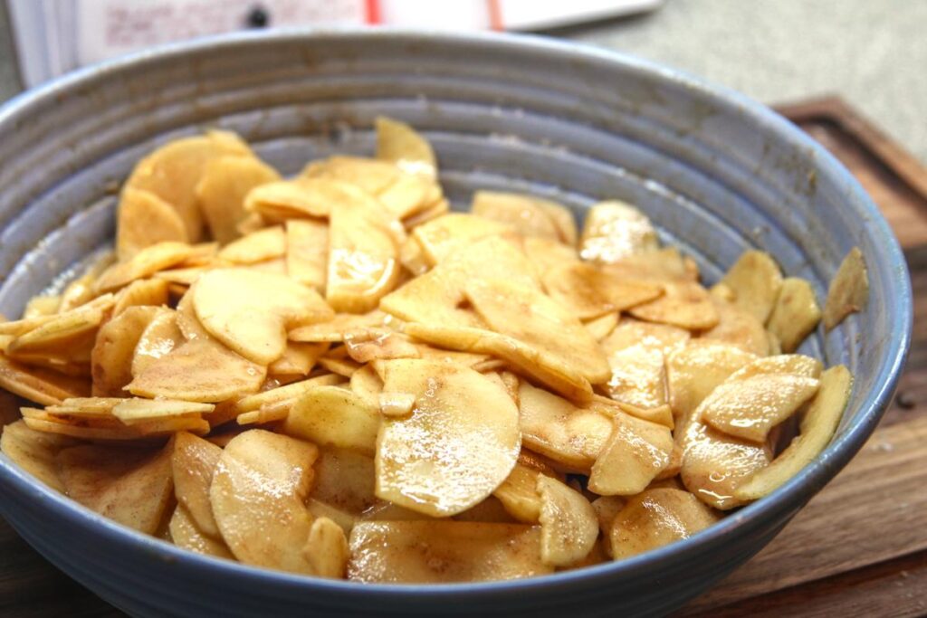A purple bowl of apple slices. The slices are covered in a mix of flour and cinnamon.