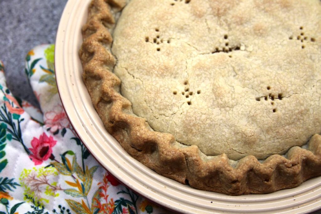 A close-up of a baked pie sitting on the counter next to a hot pad with a floral pattern.