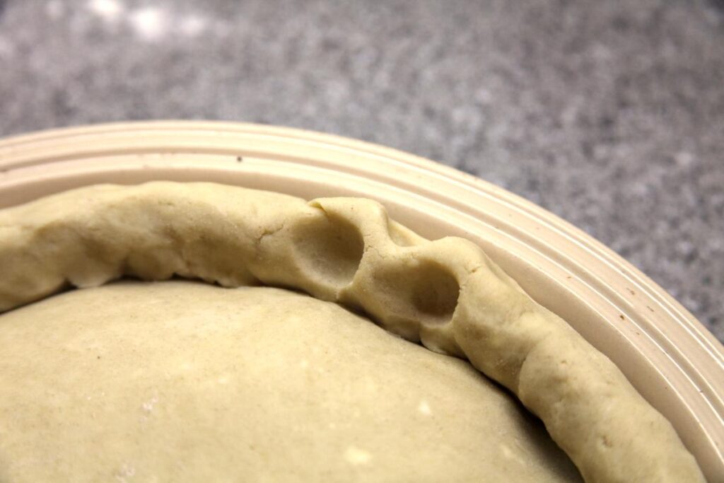 A close-up of the edge of a pie crust showing two indents on the inside and three on the outside. These indents form folds in the crust.