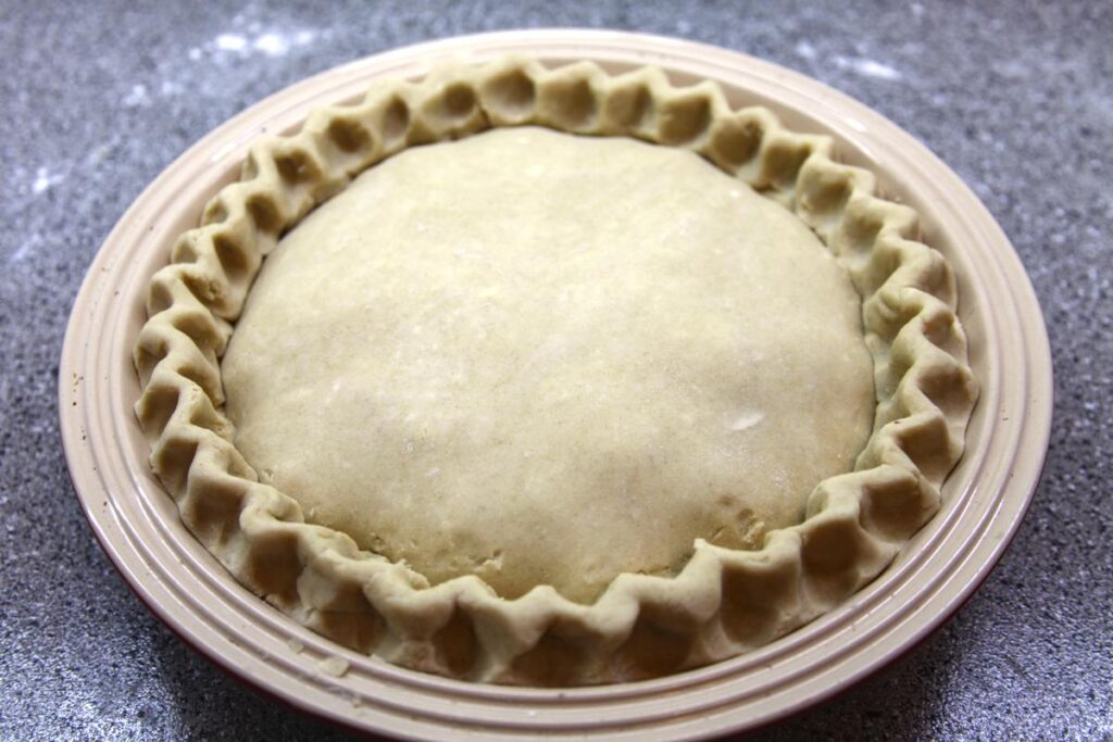 An unbaked pie sits on a countertop. The edges of the pie have a wavy pattern.