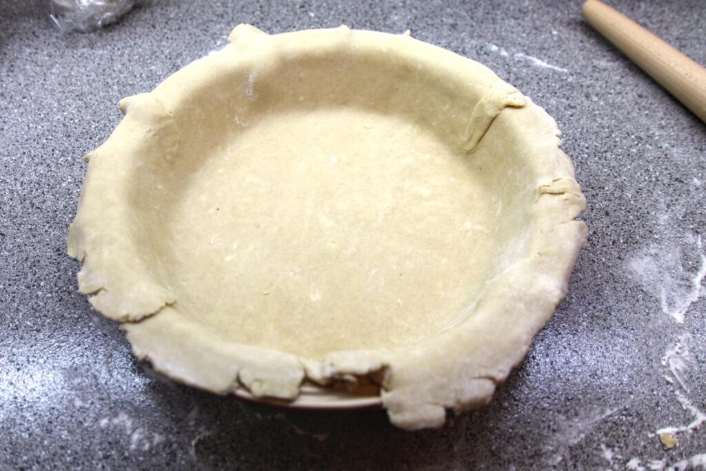 A pie plate sits on a counter. Pie crust has been arranged inside the pie plate so that the edges drape very slightly over the lip of the plate.