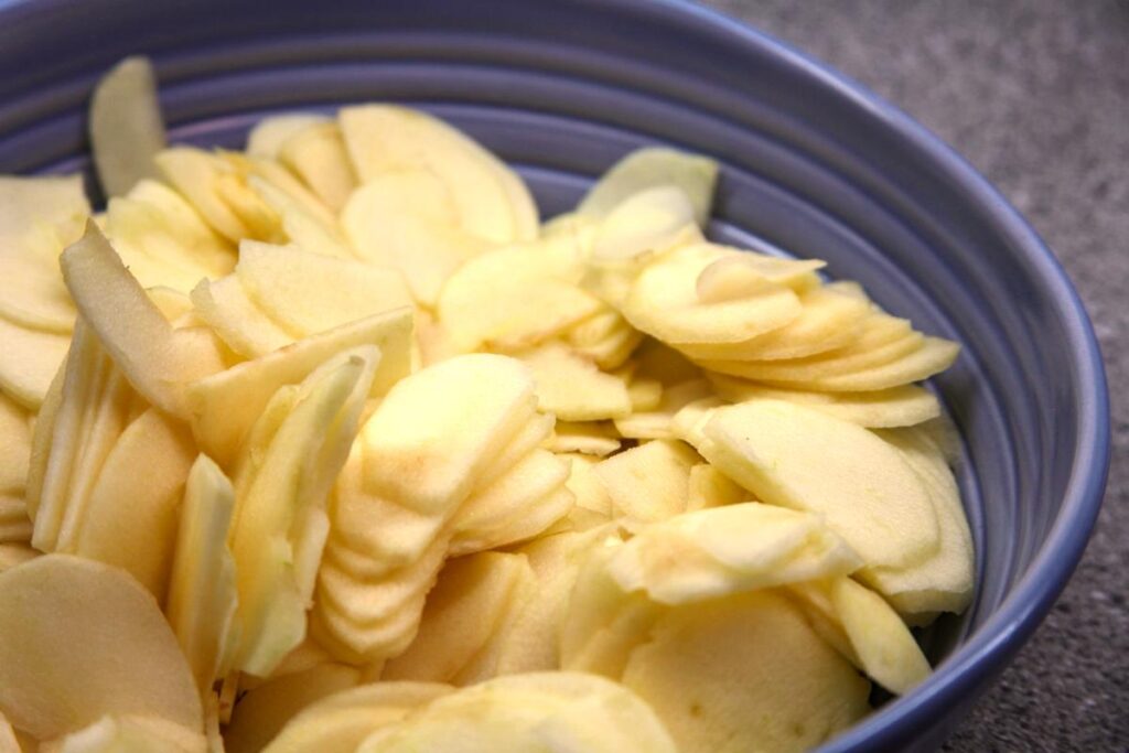 A close-up of a purple bowl filled with thinly sliced apples.